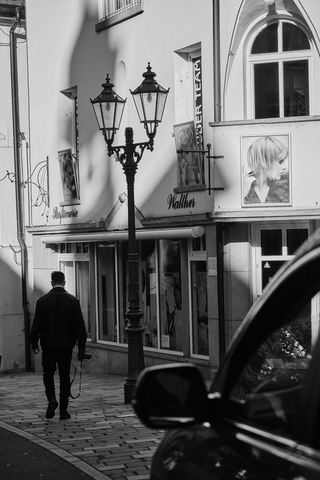 Silhouette of a man in a long coat and hat walking away under a streetlamp